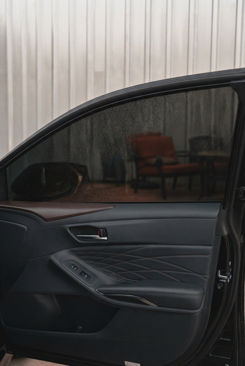 A person applying removable ceramic window tint to a car window in a driveway.