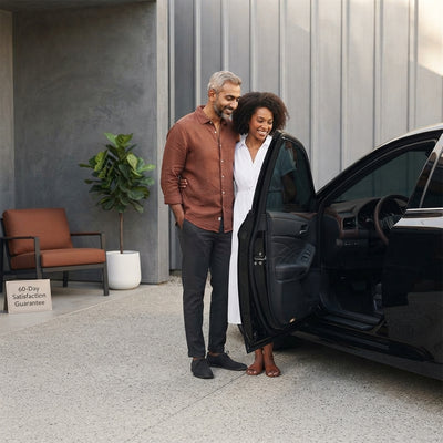 A diverse couple standing by a modern car with premium ceramic window tint applied, set in a clean, sunlit outdoor space.